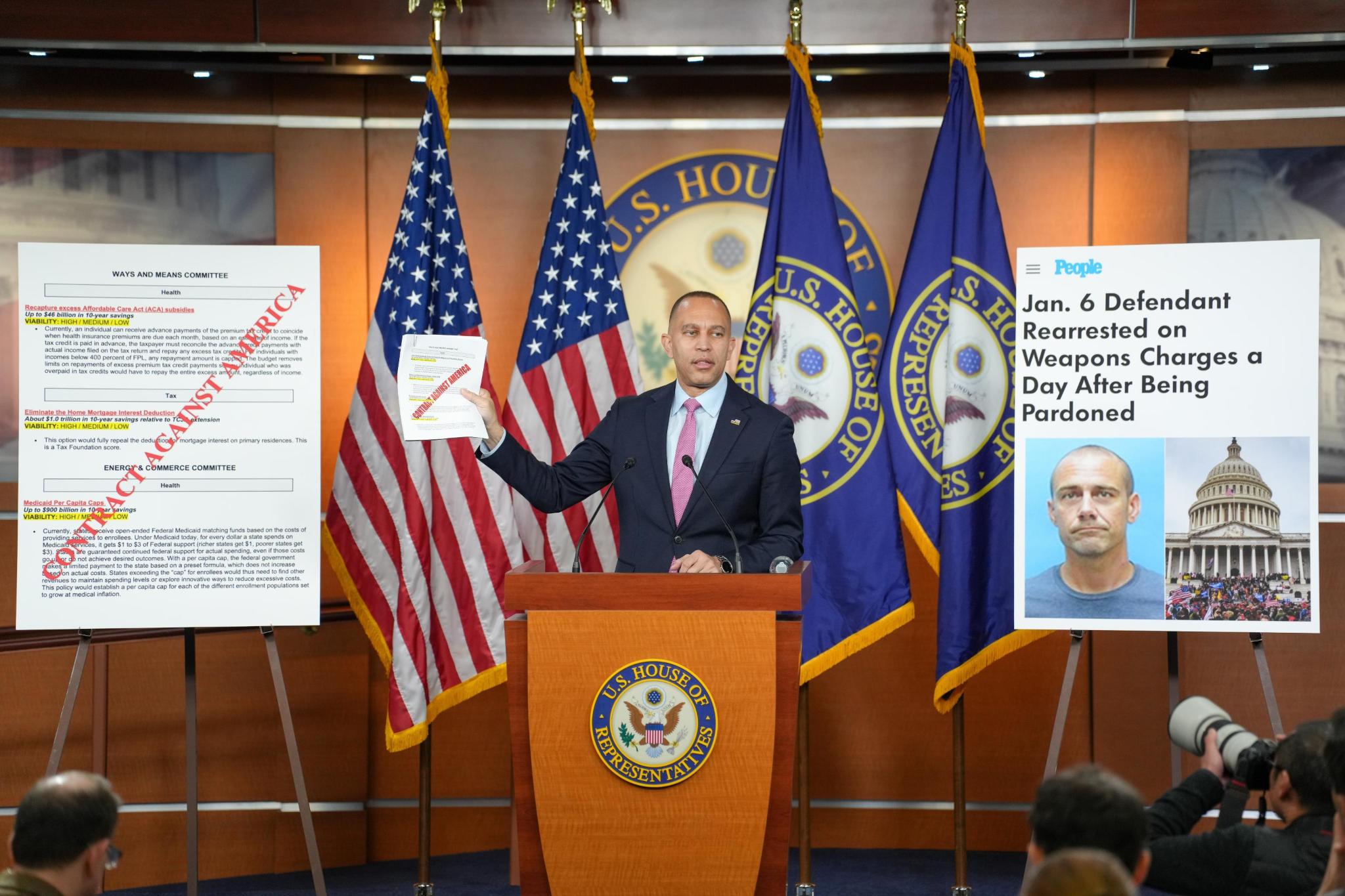 Leader Jeffries holding up a sheet of paper with the words "Contract Against America" on it, next to a poster version and a poster with a People Magazine headline: "Jan. 6 Defendant Rearrested on Weapons Charges a Day After Being Pardoned"