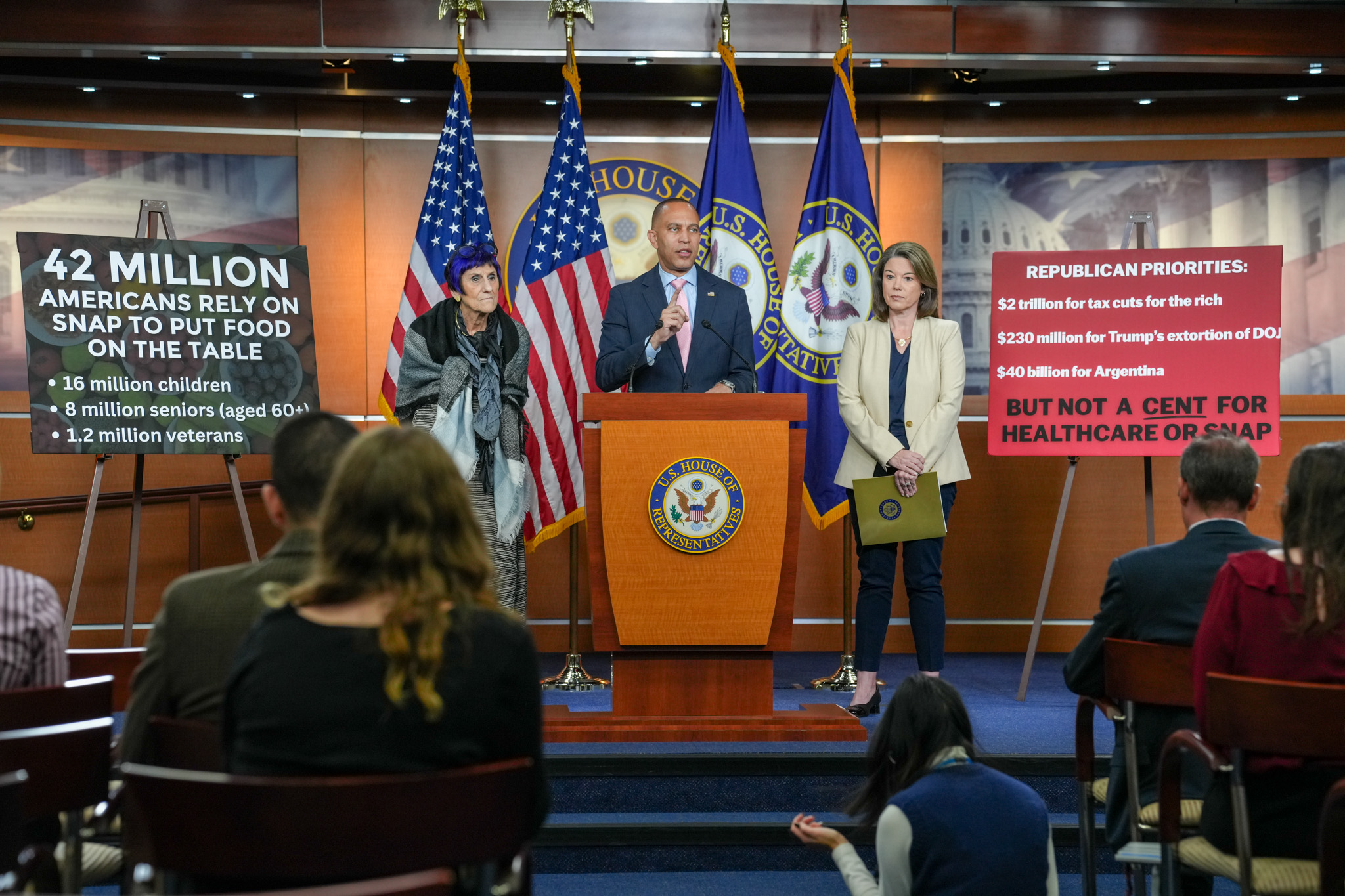 From left to right, Rep. Rosa DeLauro, Leader Jeffries, Rep. Angie Craig speaking at press conference in between signs reading "42 million Americans rely on SNAP to put food on the table, 16 million children, 8 million seniors (aged 60+), 1.2 million veterans and another reading "Republican Priorities: $2 trillion for tax cuts for the rich, $230 million for Trump's extortion of DOJ, $40 billion for Argentina BUT NOT A CENT FOR HEALTHCARE OF SNAP"