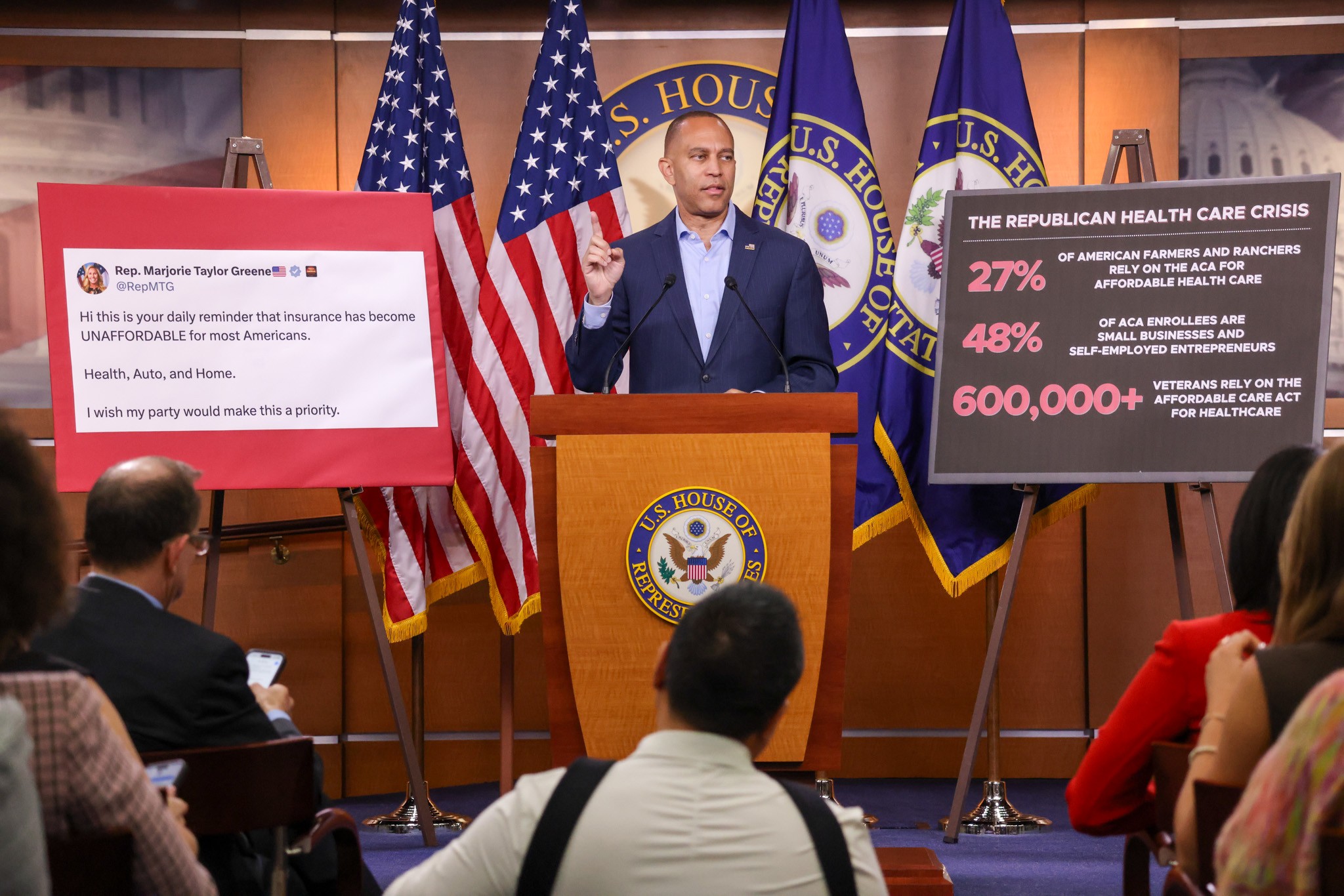 Leader Jeffries speaking at weekly press conference between a poster of a Marjorie Taylor Greene tweet and a poster with stats about the impacts of the Republican Healthcare Crisis
