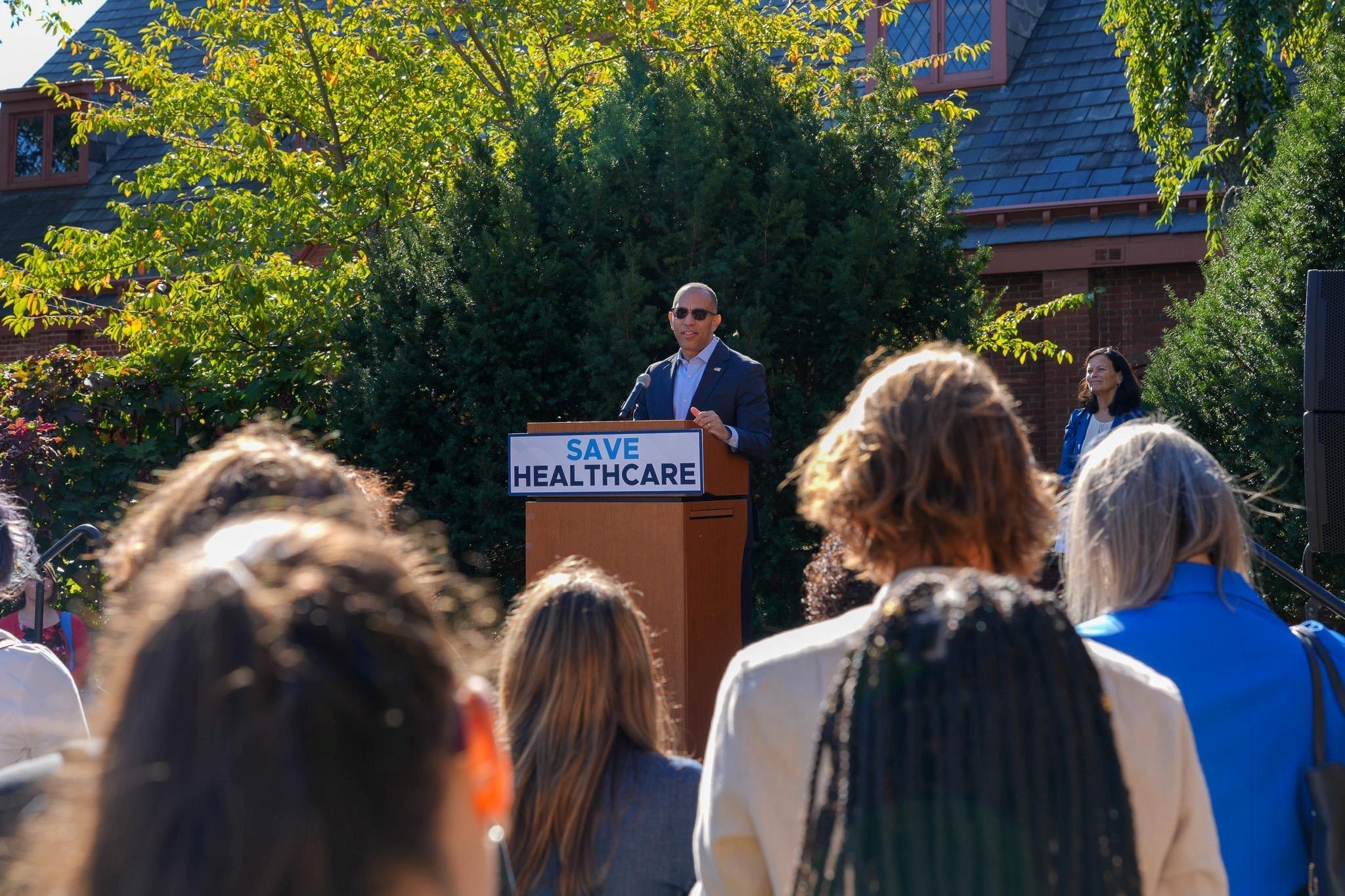 Leader Jeffries speaking at a rally behind a podium and sign reading "Save Healthcare"