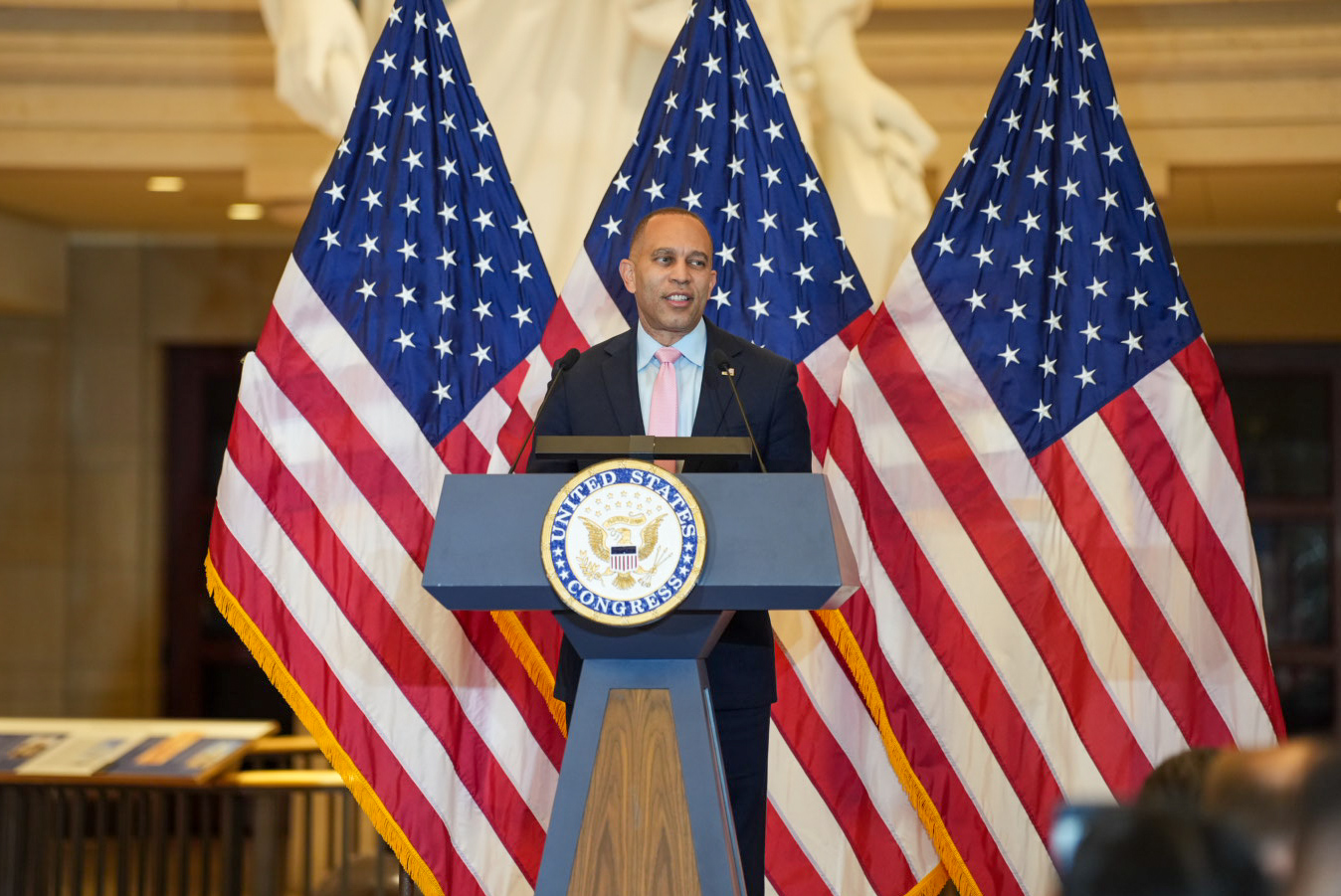 Leader Jeffries speaking behind a podium in Emancipation Hall and in front of three American flags