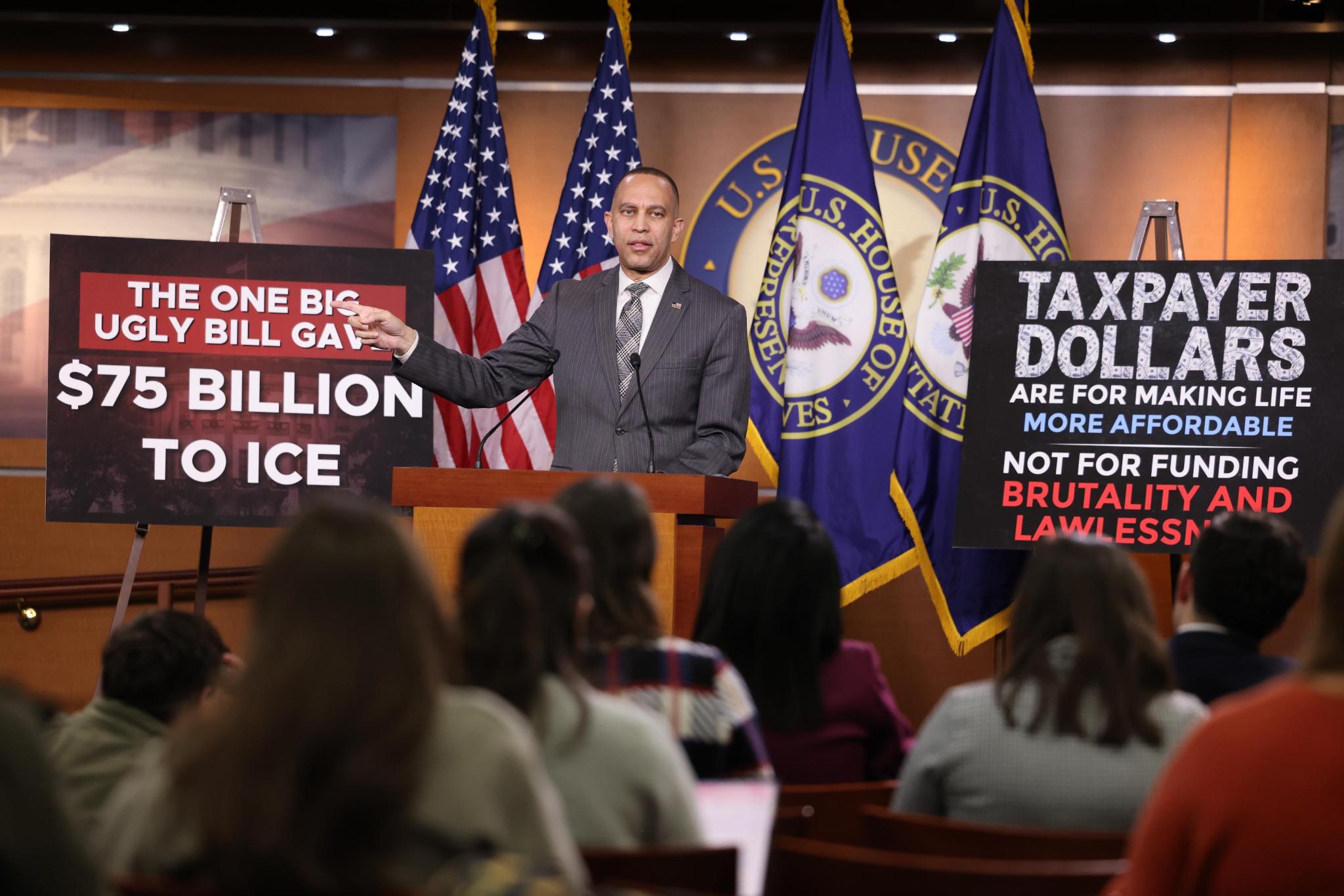 Leader Jeffries speaking at weekly press conference with signs reading "The One Big Ugly Bill Gave $75 Billion to ICE" (left) and "Taxpayer Dollars Are For Making Life More Affordable, Not For Funding Brutality and Lawlessness" (right)