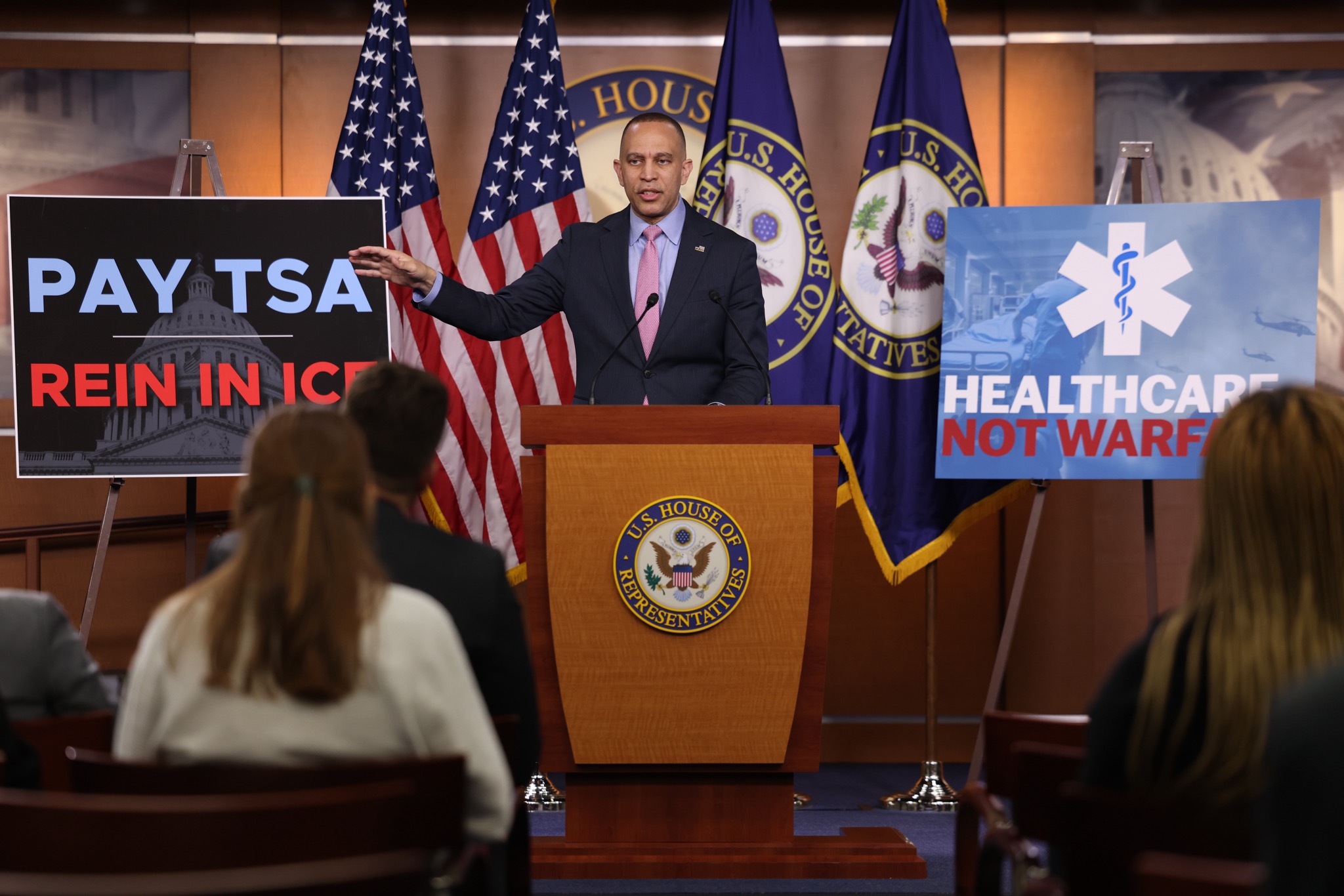 Leader Jeffries Speaking at Weekly Press Conference in between posters that read "Pay TSA Rein In Ice" and "Healthcare Not Warfare"