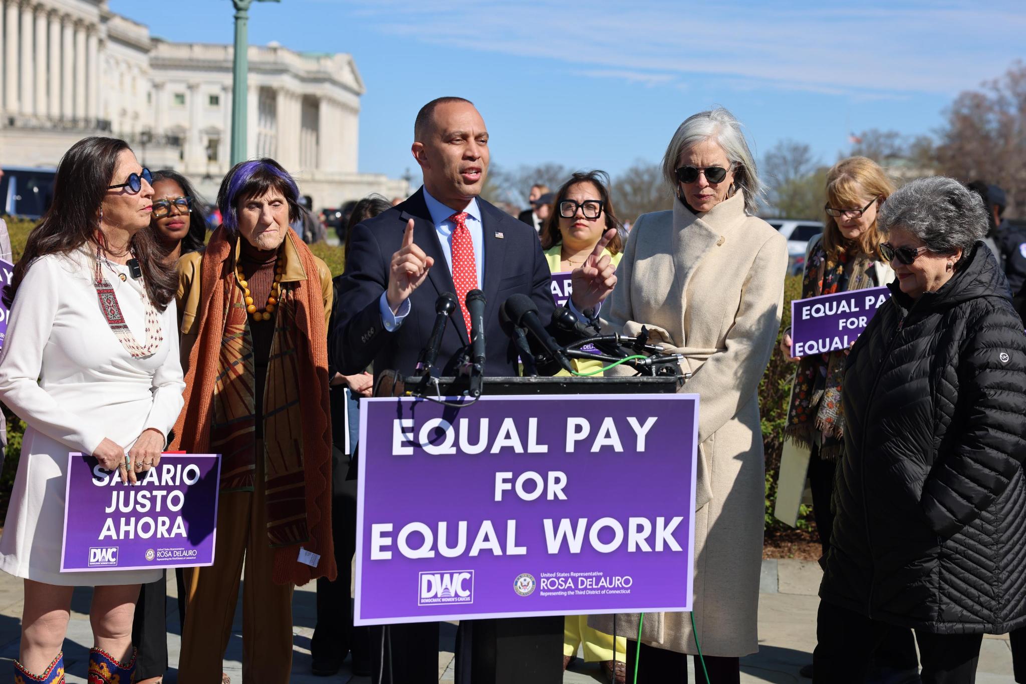 Leader Jeffries speaking behind a purple podium sign reading "Equal Pay for Equal Work"