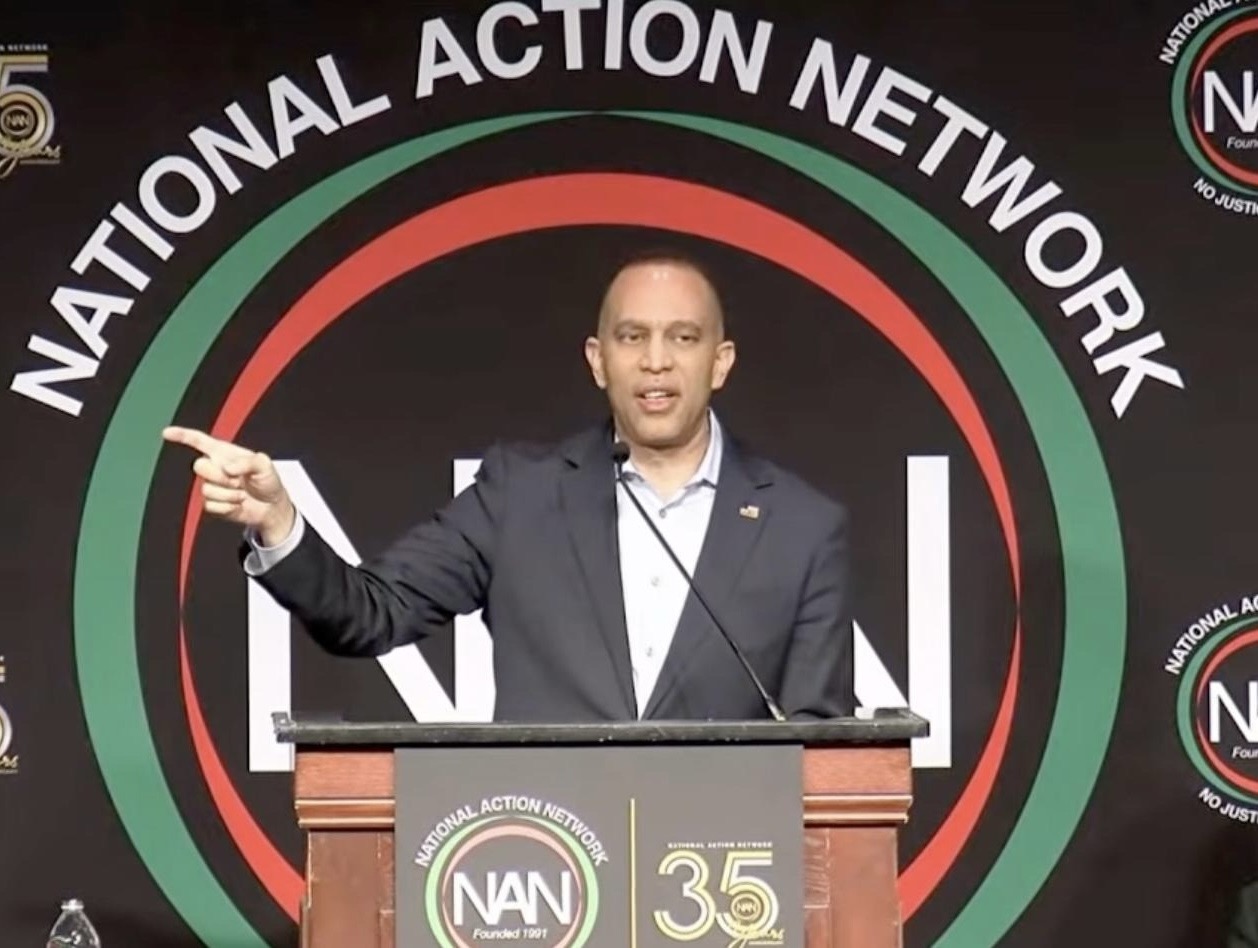 Leader Jeffries speaking from behind a podium in front of the National Action Network logo