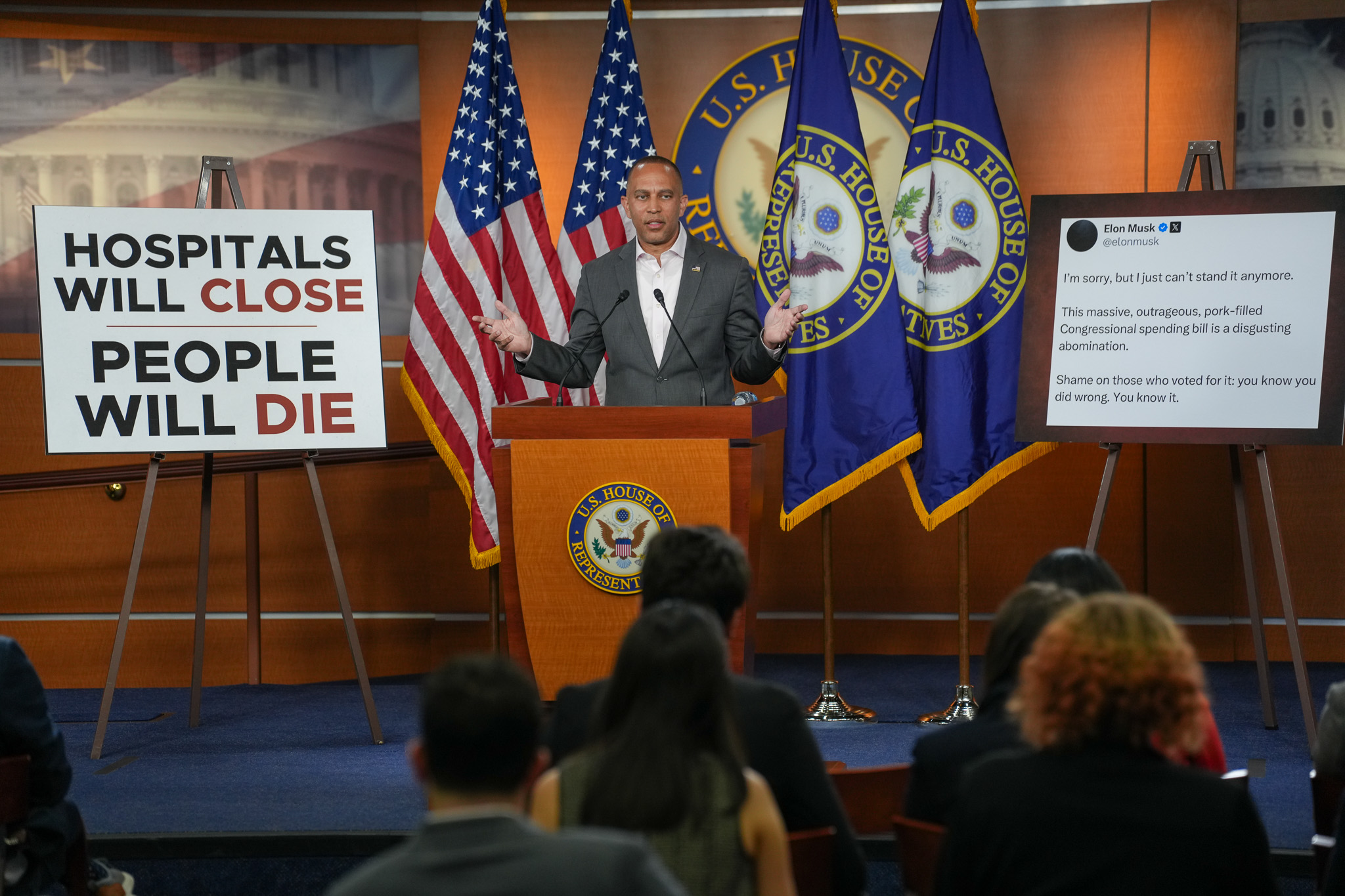 Leader Jeffries Speaking at Weekly Press Conference between a poster reading "Hospitals Will Close, People Will Die" and another displaying a tweet from Elon Musk: I’m sorry, but I just can’t stand it anymore. This massive, outrageous, pork-filled Congressional spending bill is a disgusting abomination. Shame on those who voted for it: you know you did wrong. You know it.