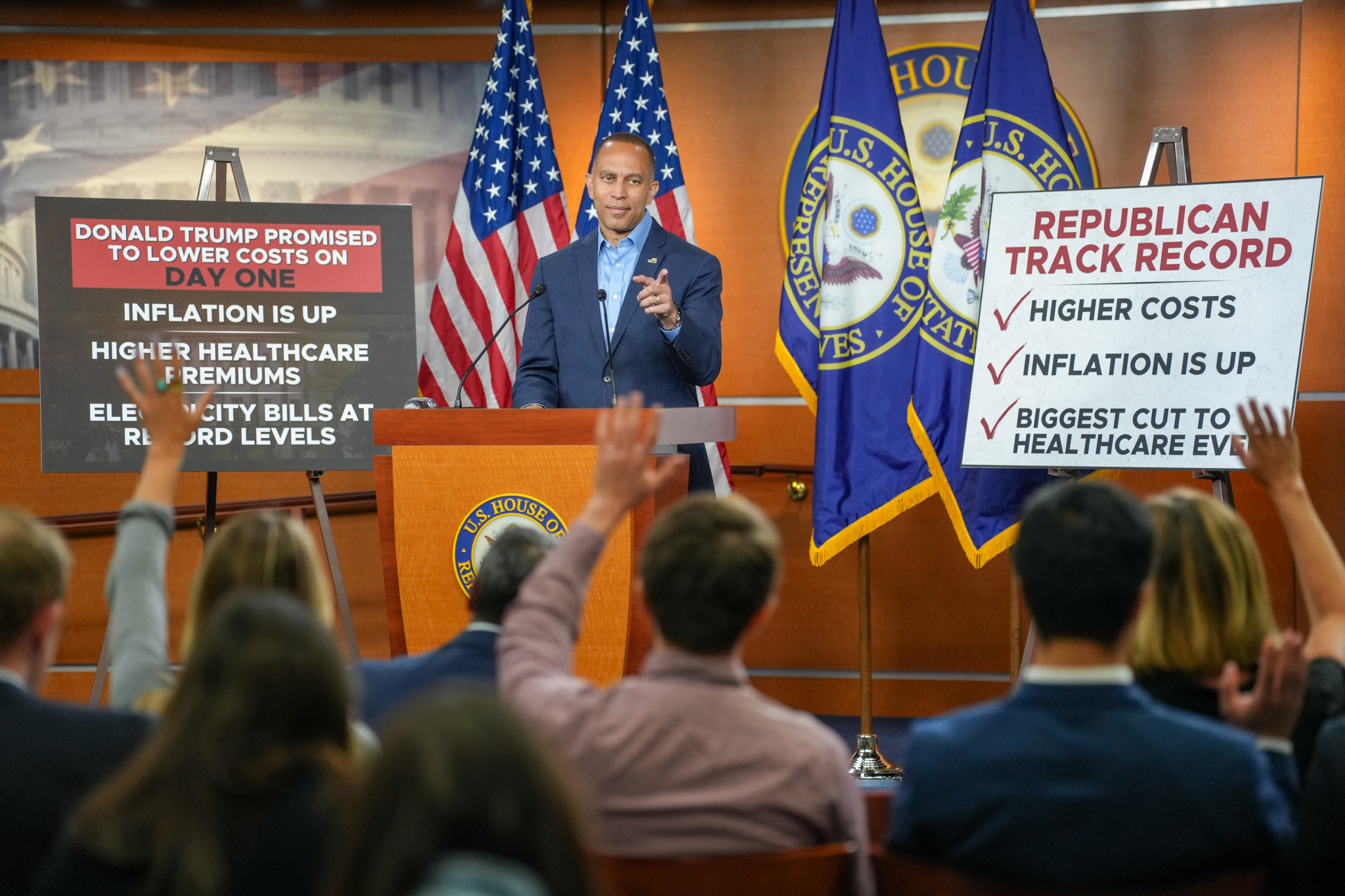 Leader Jeffries pointing at reporters while standing in between signs that read, "Donald Trump Promised to Lower Costs on Day One/Inflation is Up/Higher Healthcare Premiums/Electricity Bills at Record Levels" and "Republican Track Record/Higher Costs/Inflation is Up/Biggest Cut to Healthcare Ever"