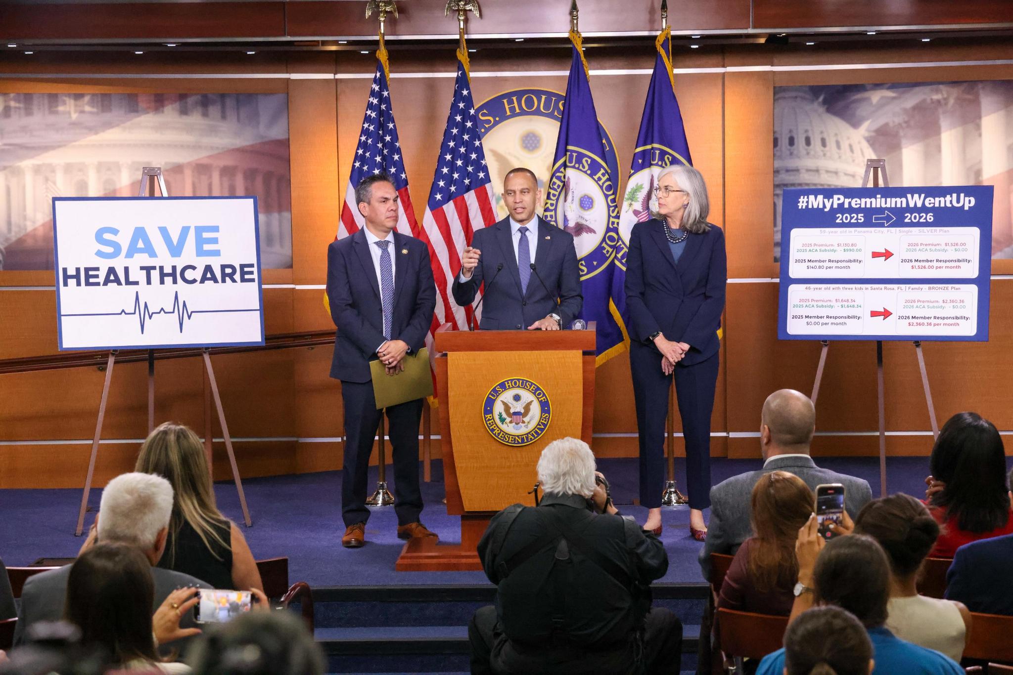 Chair Pete Aguilar (left), Leader Jeffries (center) and Whip Katherine Clark (right) speaking at press conference in between signs reading "Save Healthcare" and a description of healthcare premium increases
