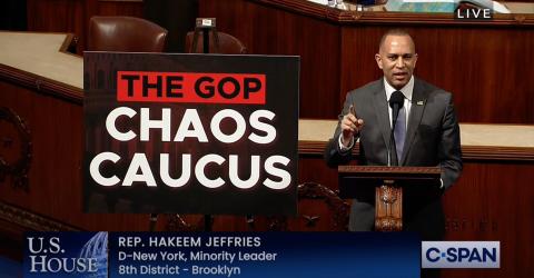 Leader Jeffries speaking on the House Floor with a sign reading THE GOP CHAOS CAUCUS
