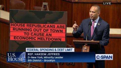 Leader Jeffries speaking on the House Floor next to a sign reading "House Republicans are running out of town to cause an economic meltdown"