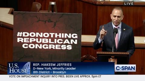 Leader Jeffries speaking on the House Floor with a sign reading #DONOTHINGREPUBLICANCONGRESS