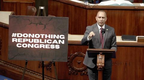 Leader Jeffries speaking on the House Floor with a sign reading #DONOTHINGREPUBLICANCONGRESS