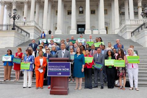 Leader Jeffries speaking on the East Capitol Steps behind a sign reading 'Reproductive Freedom Now.' Behind him are members of the House Democratic Caucus